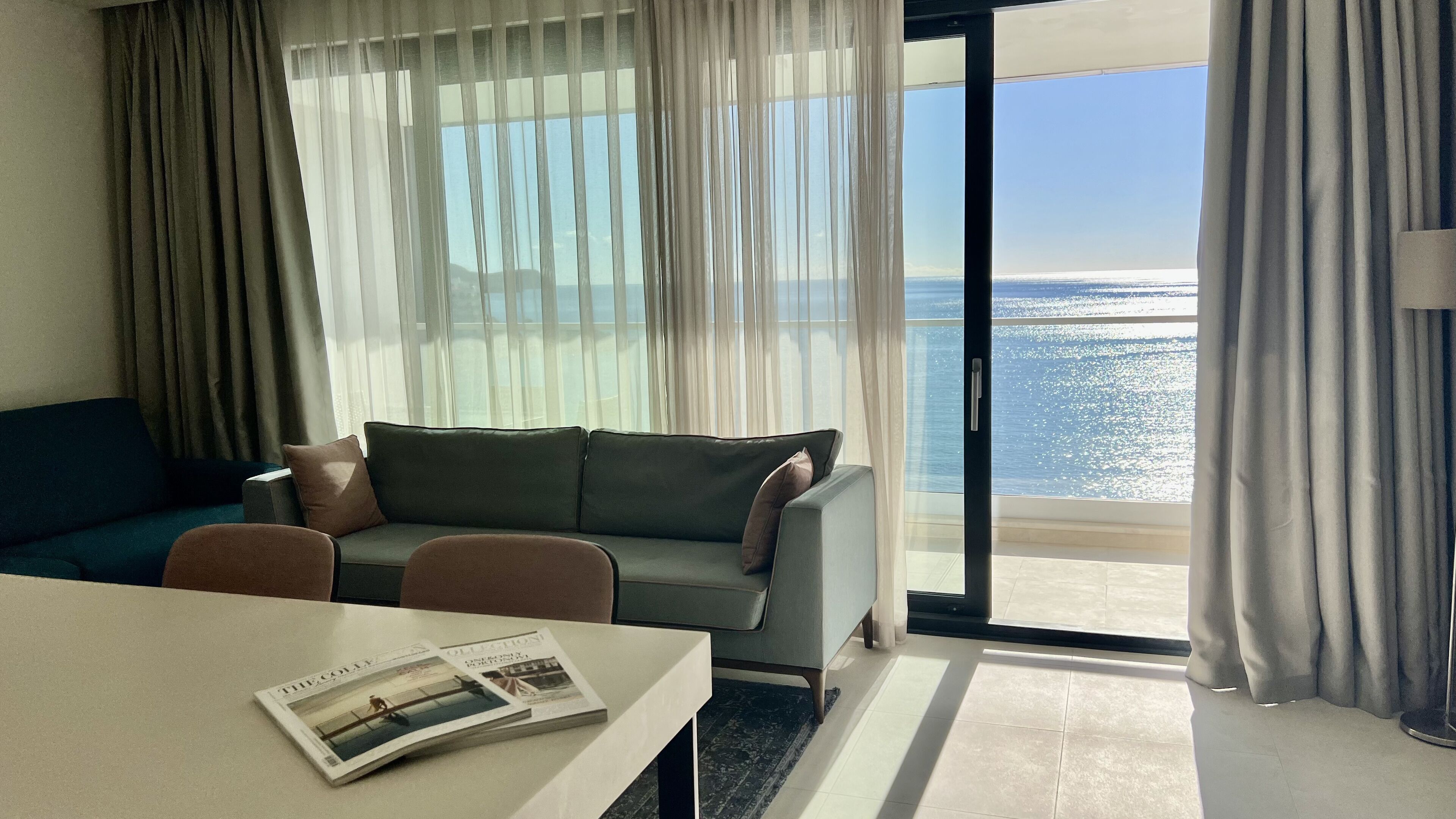 A modern hotel room with a sofa, a dining table, and a view of the ocean.