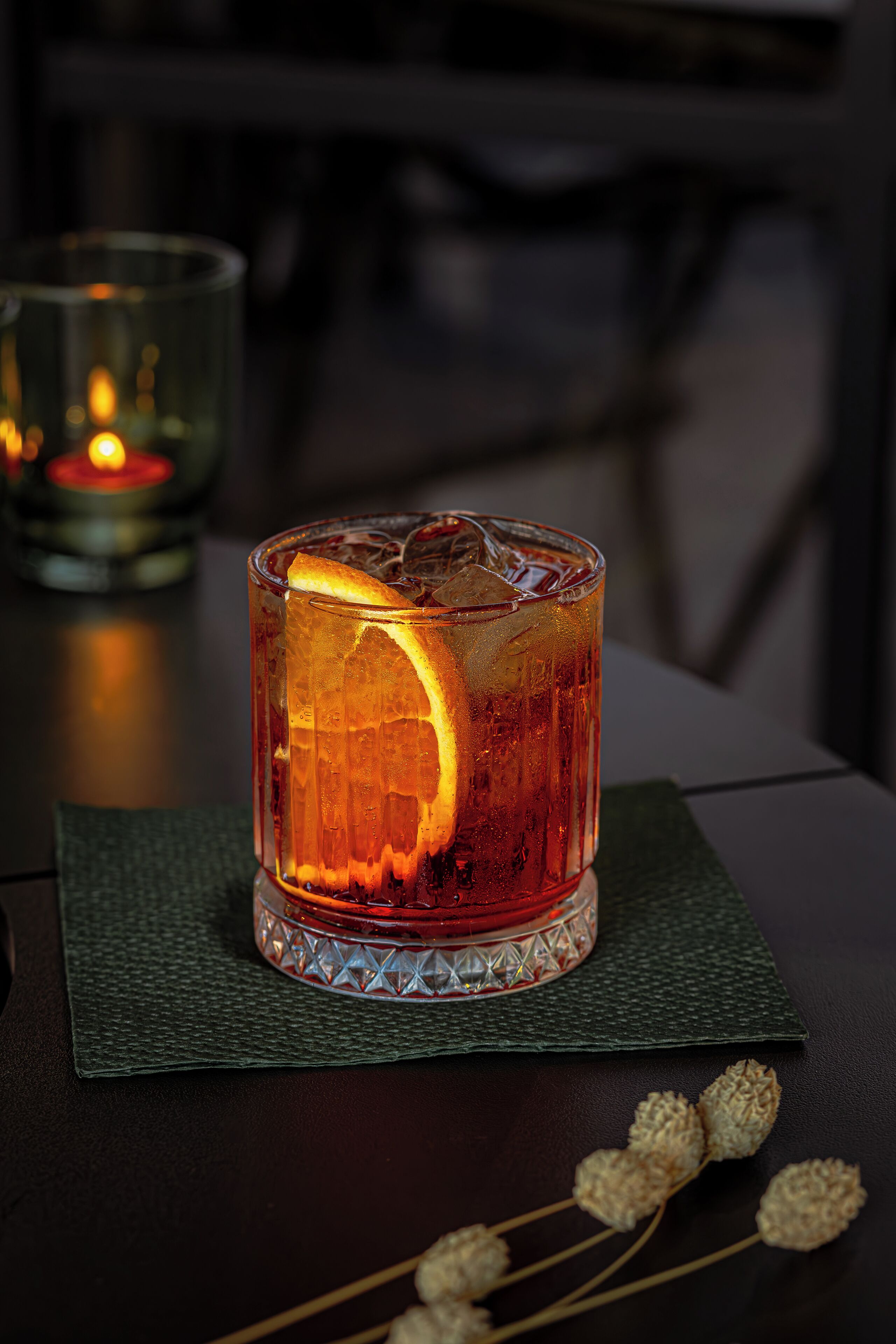 A glass of amber-colored beverage with an orange slice, placed on a textured mat.