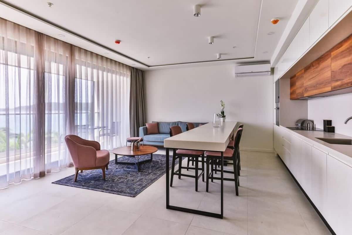 A modern living room with a dining table, sofa, and a large window with curtains.