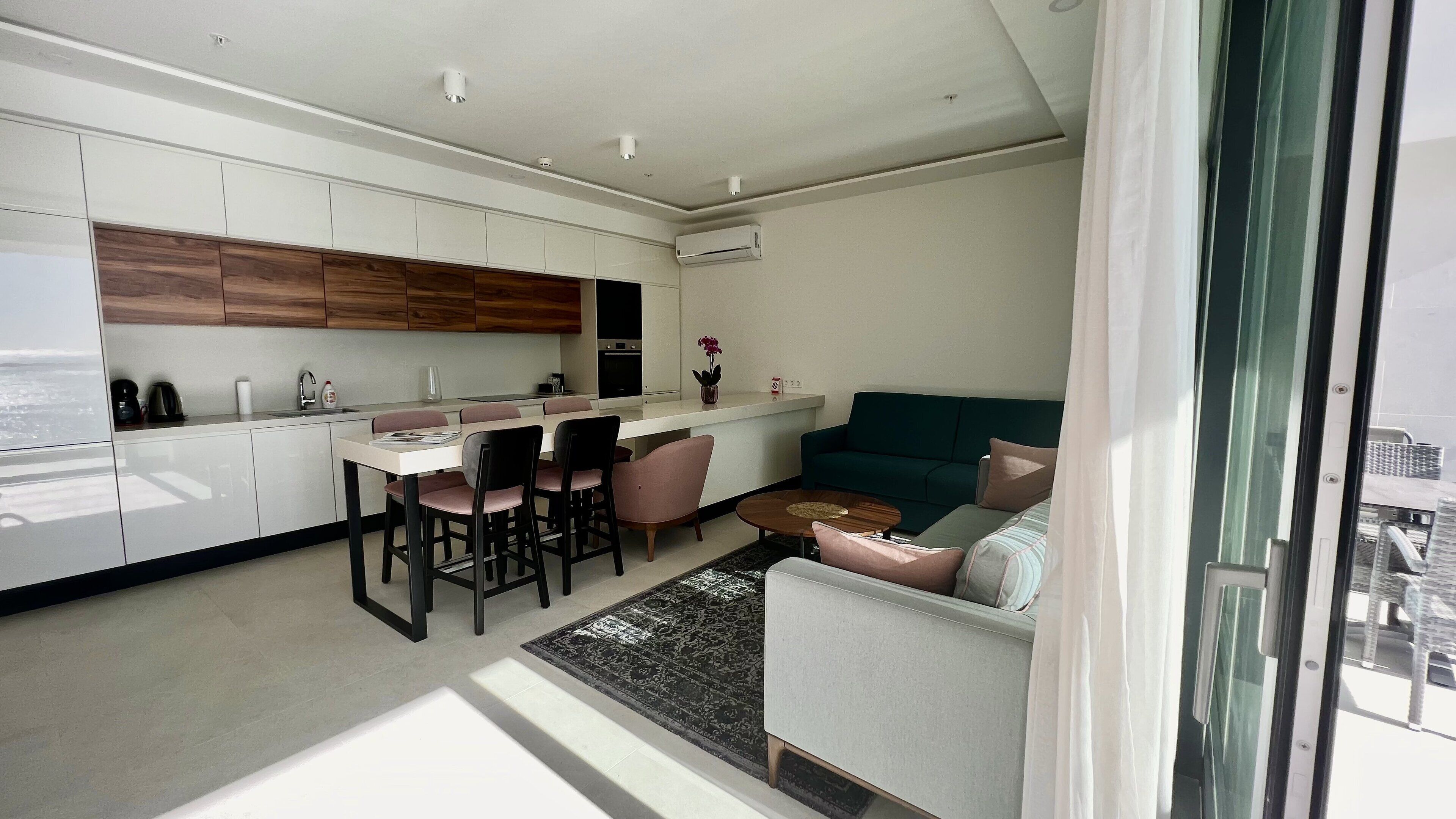 A modern kitchen with white cabinets, a dining area with a table and chairs, and a living area with a sofa and a coffee table.