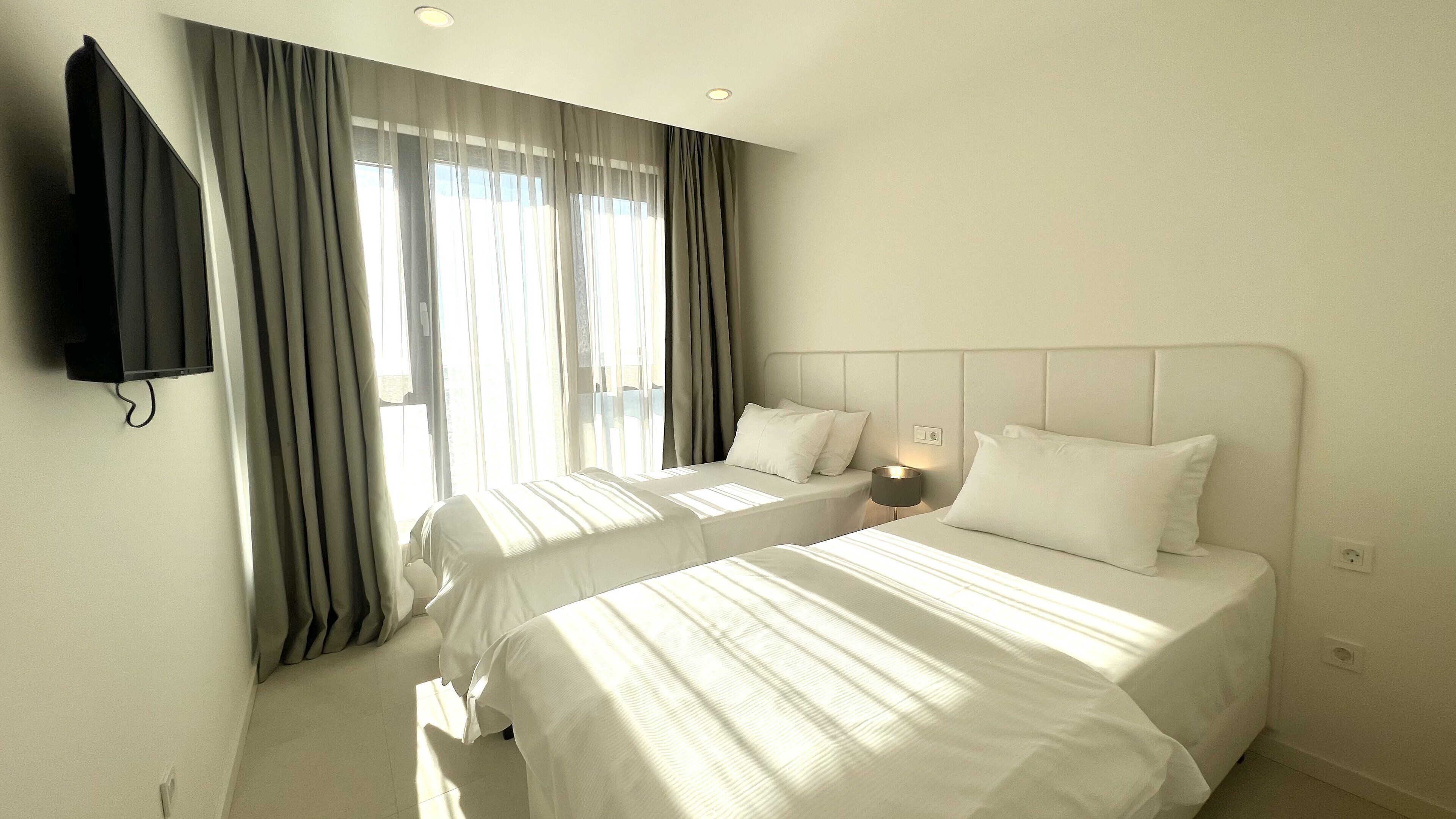 A hotel room with two beds, a TV mounted on the wall, and a window with curtains.