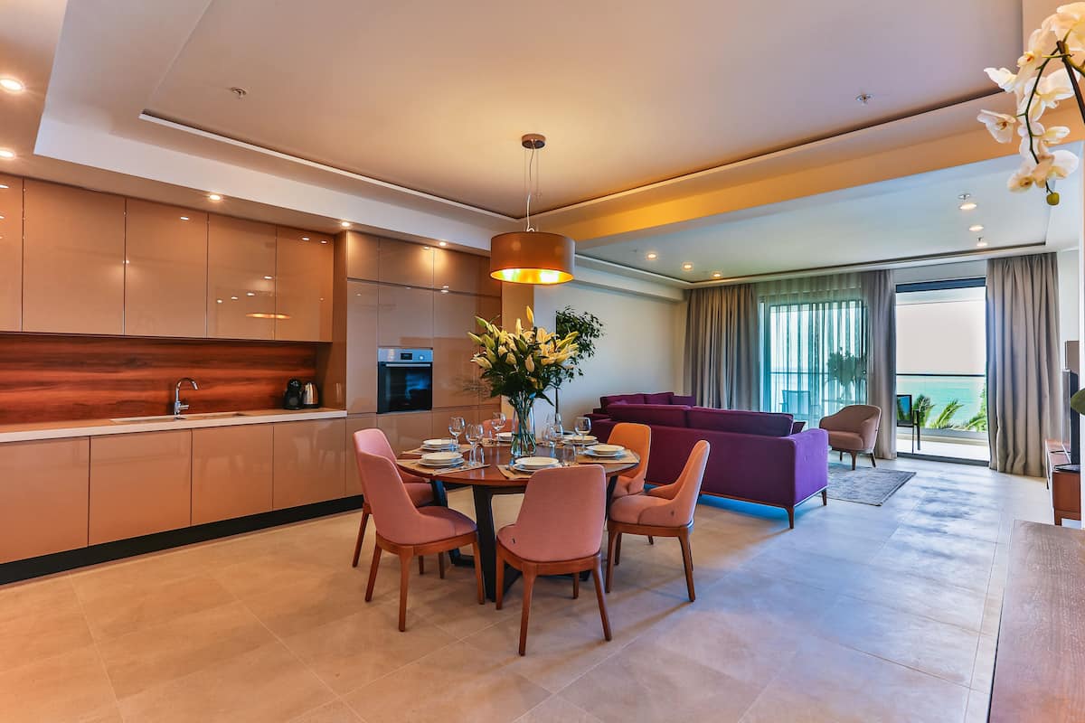 A modern kitchen with a dining area, a purple sofa, and a view of the ocean.
