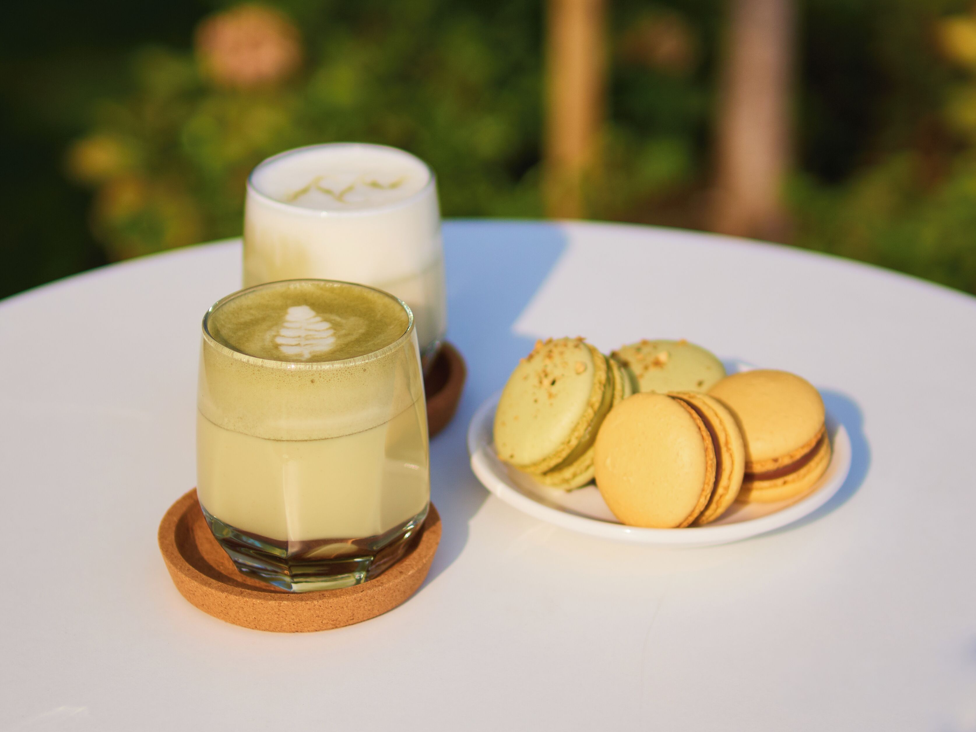 Due bicchieri di una bevanda chiara su un tavolo bianco con un piatto di macarons gialli.