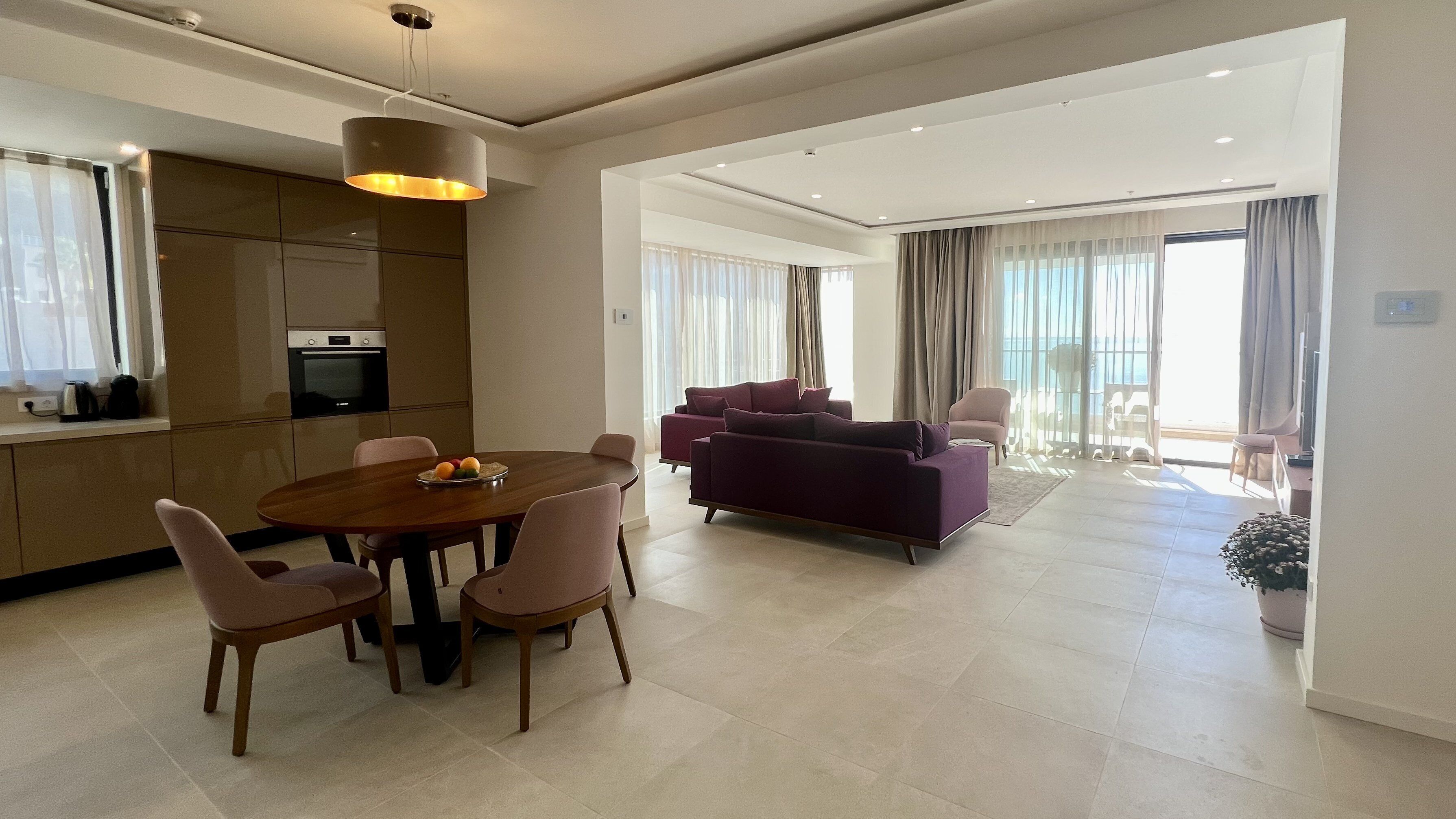 A modern living room with a dining area, a kitchen, and a balcony with curtains.