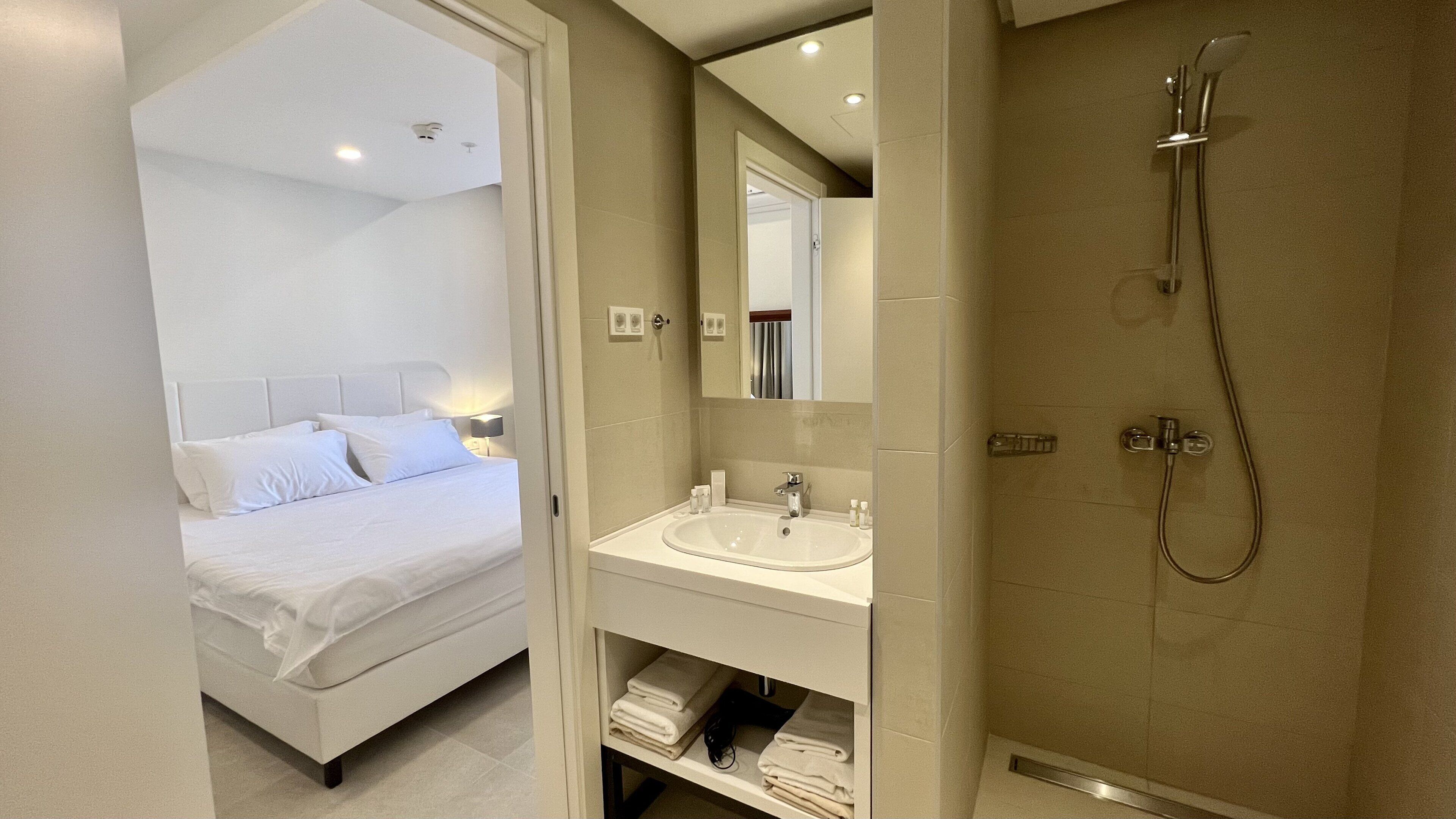 A modern bathroom with a shower, sink, and a bed with white linens.