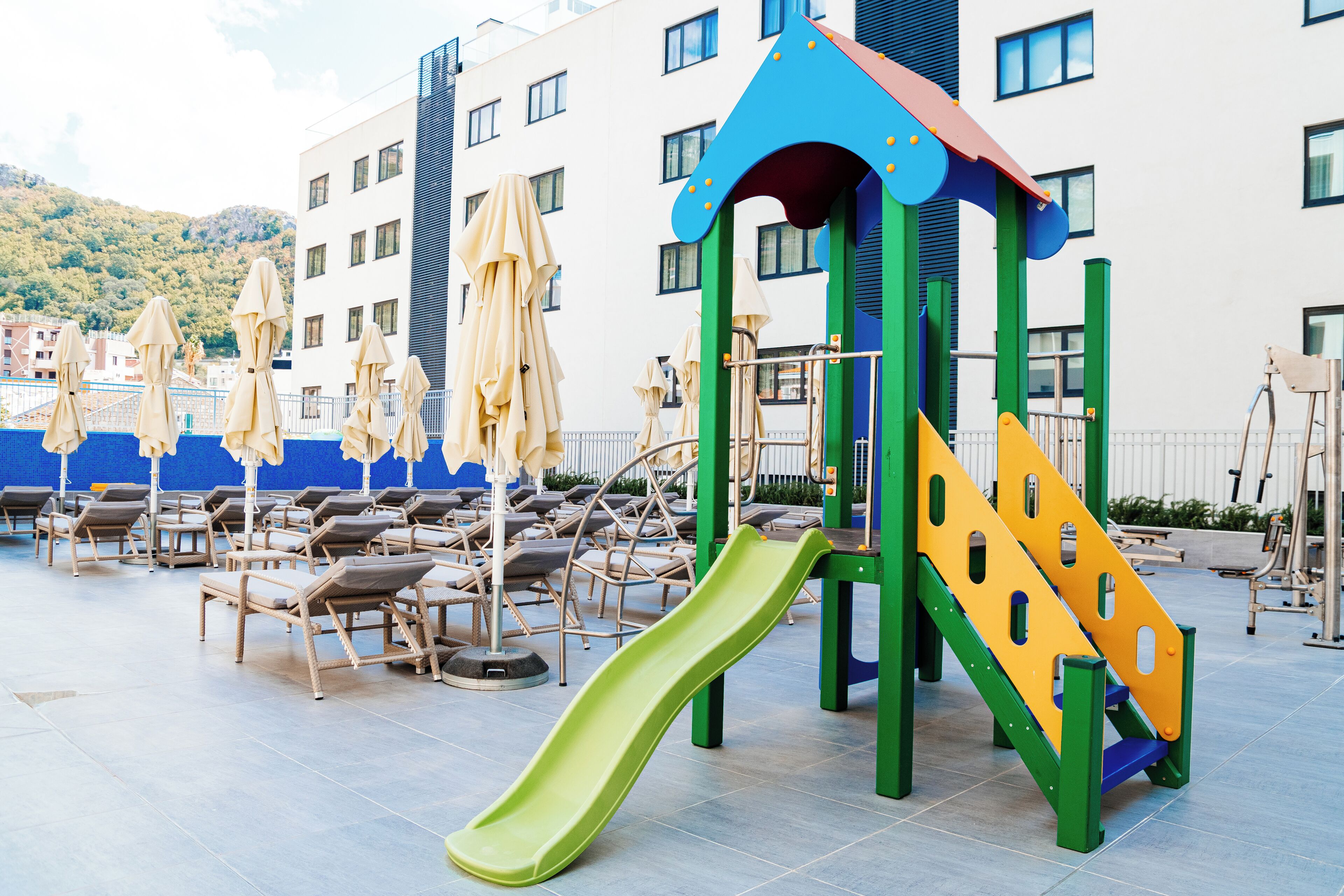 A children's play area with a slide, surrounded by lounge chairs and umbrellas.
