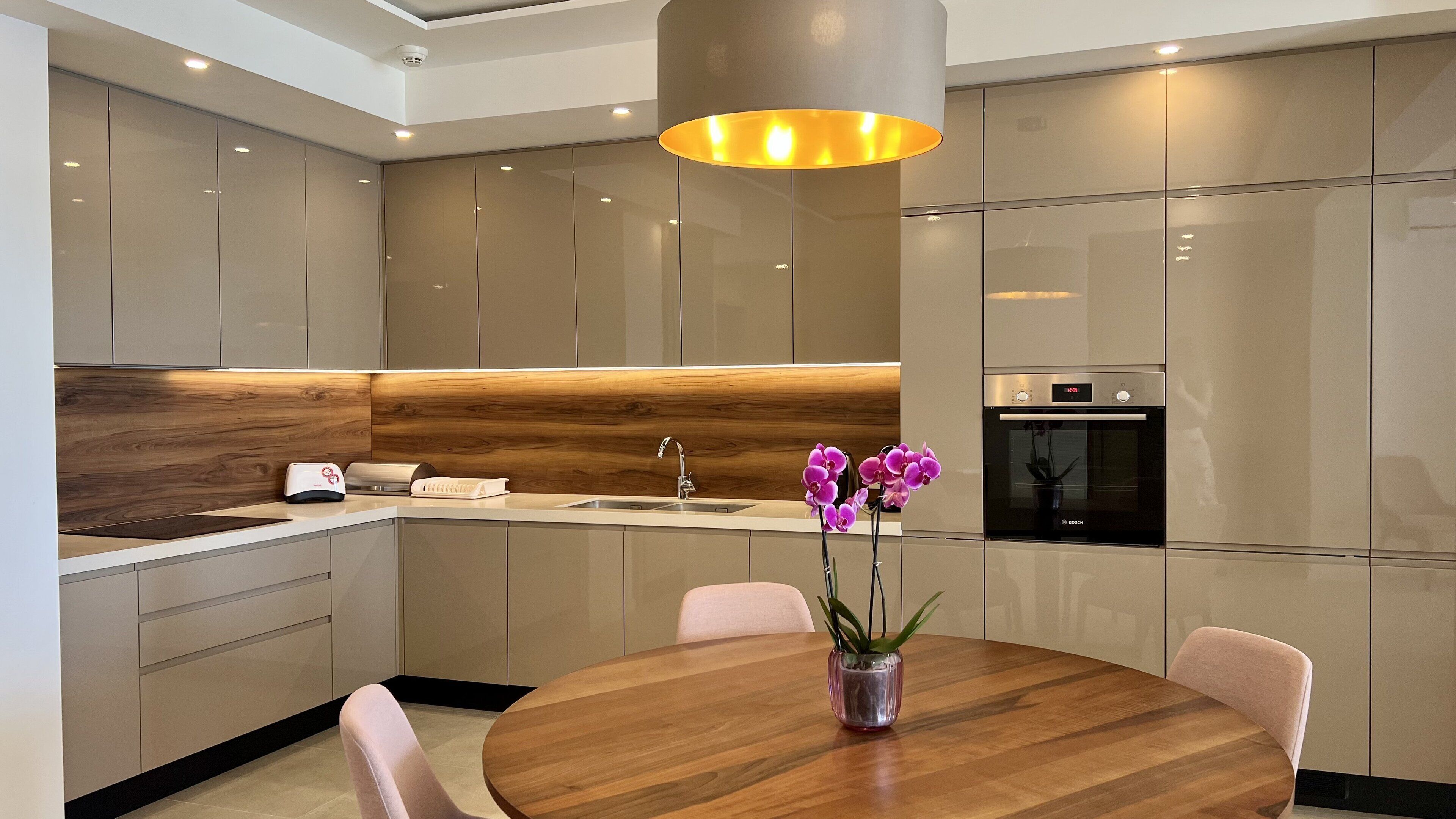 A modern kitchen with a wooden accent wall, a Bosch oven, and a round dining table with chairs.