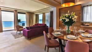 Una sala de estar moderna con un ventanal grande, un sofá morado, una mesa de comedor lista para cuatro personas y vistas al mar.