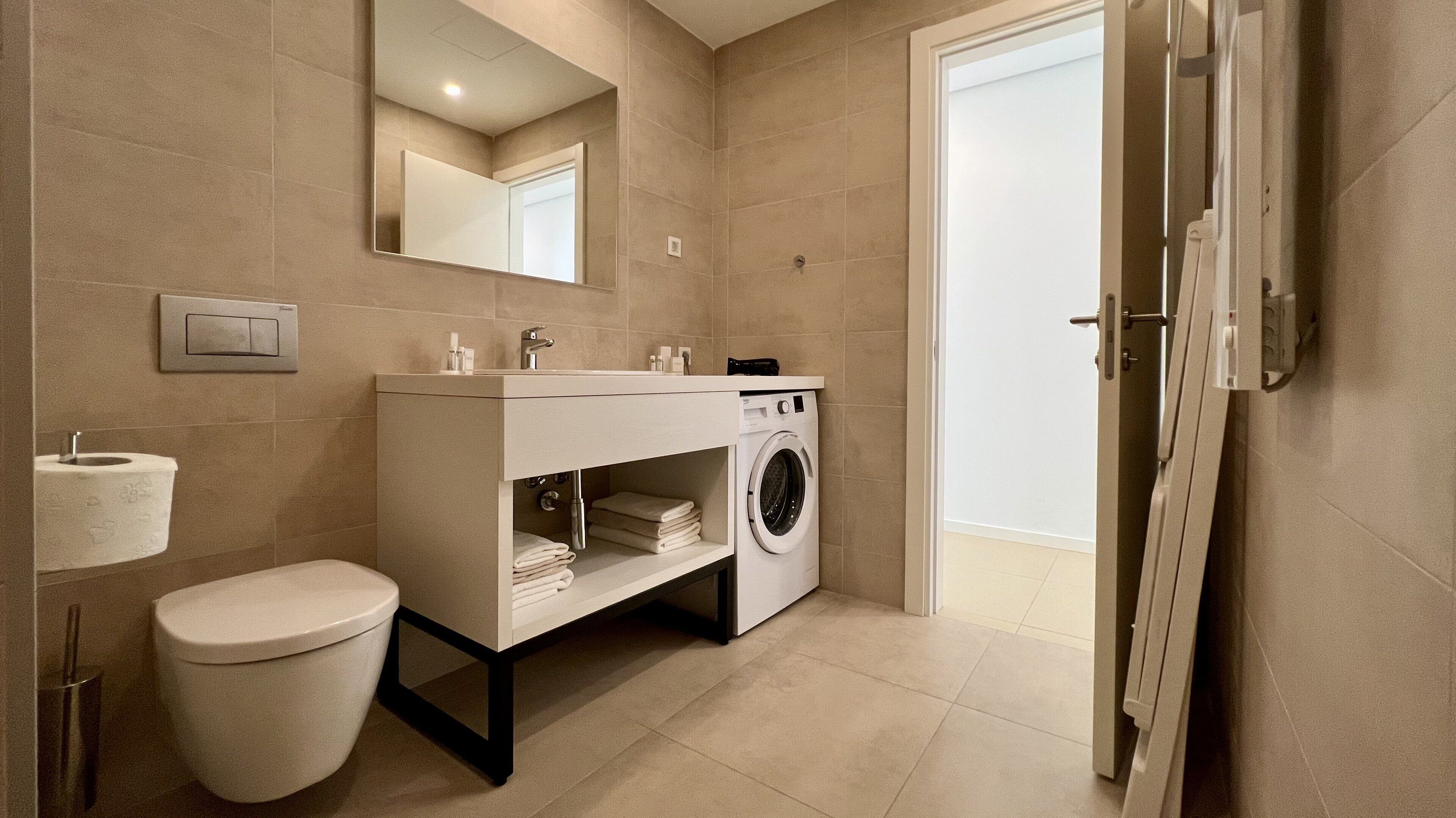 A modern bathroom with a toilet, sink, mirror, and built-in washing machine.
