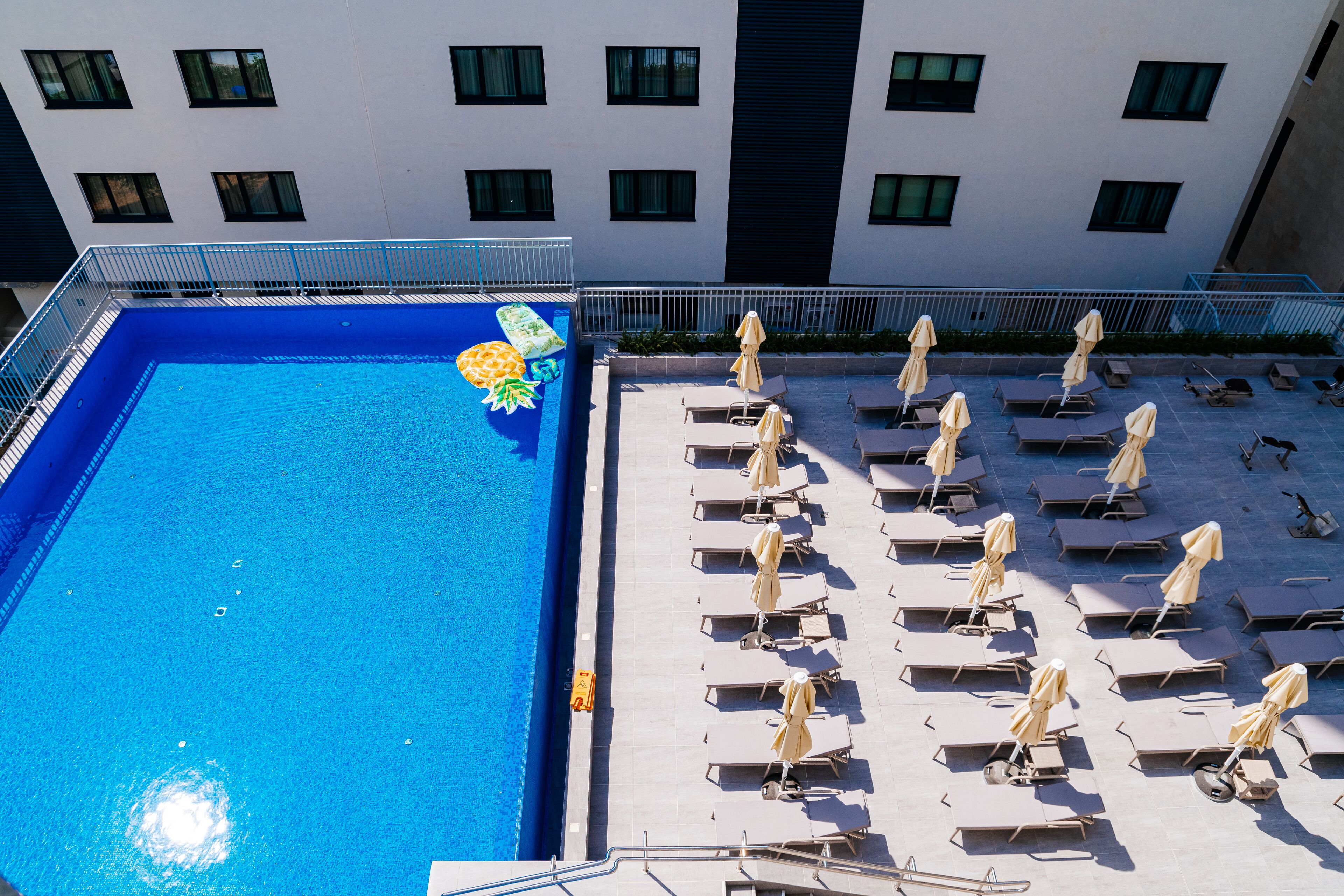 Ein Pool auf dem Dach mit klarem, blauem Wasser, umgeben von Liegestühlen und Sonnenschirmen, mit einem Gebäude mit mehreren Fenstern im Hintergrund.