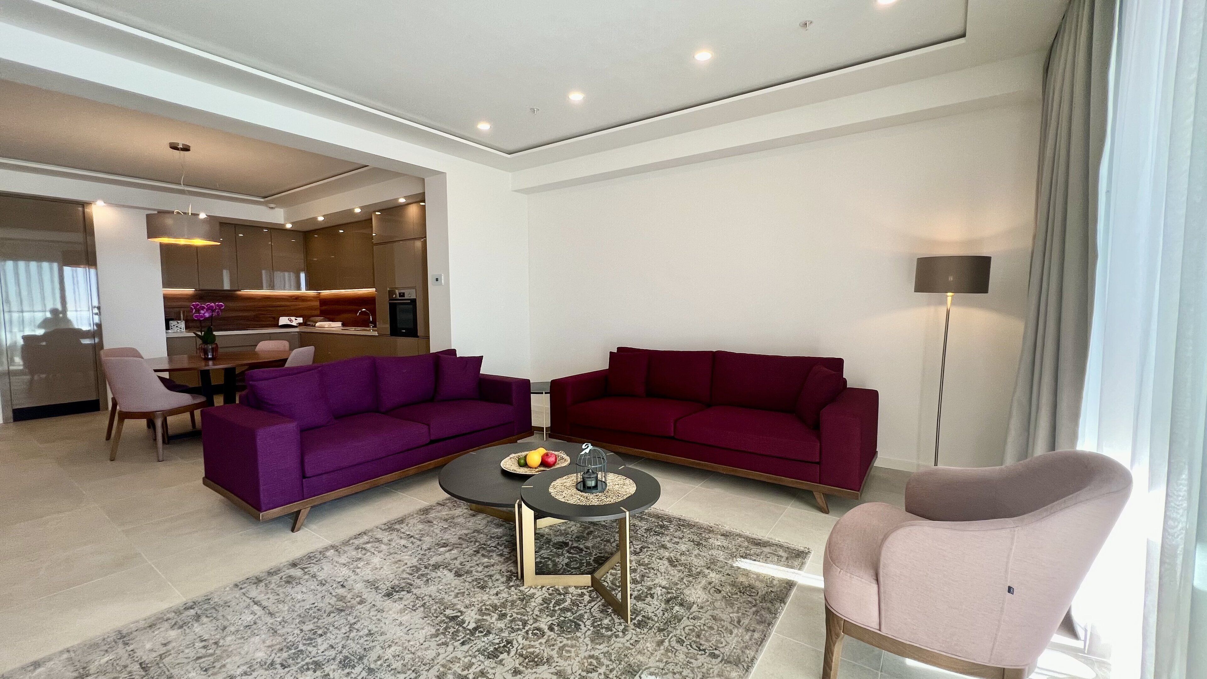 A modern living room with two purple sofas, a small round coffee table, and a pink armchair.