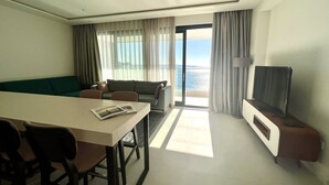 Habitación de hotel con una mesa de comedor, dos sofás, un televisor y vista al mar.