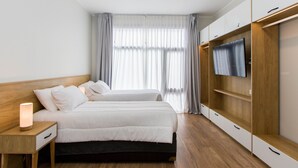 Ein modernes Hotelzimmer mit zwei Betten, einem Fernseher auf einer Holzablage und einem großen Fenster mit Vorhängen.