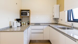 Eine kompakte Küche mit weißen Schränken, einer Granit Arbeitsplatte, einer Edelstahl-Spüle, einer Mikrowelle und einer Kaffeemaschine.