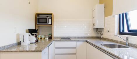 A compact kitchen with white cabinets, a granite countertop, a stainless steel sink, a microwave, and a coffee maker.