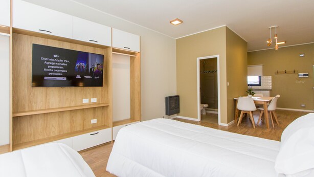 Ein Hotelzimmer mit Fernseher an der Wand, einem Schreibtisch mit Stühlen und einem Bett.