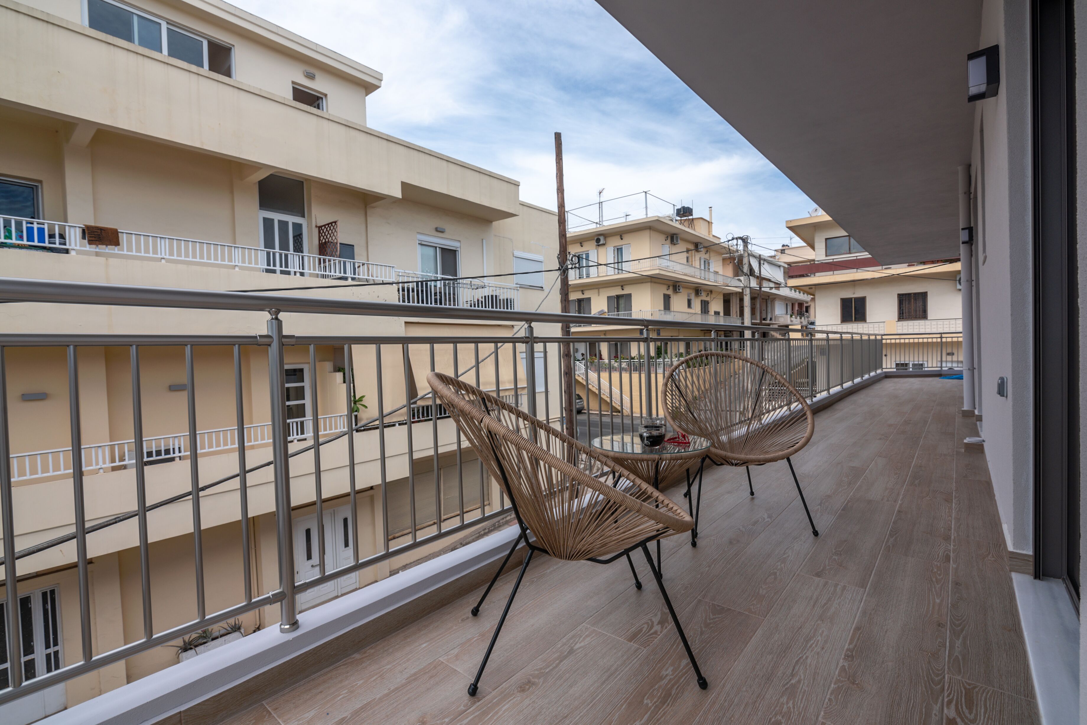 Ein Balkon mit Korbstühlen und Geländer, mit Blick auf ein Wohngebiet und mehrere Gebäude.