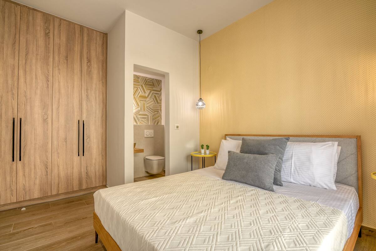 A bedroom with a large bed, a wardrobe, a small bedside table with a lamp, and a patterned wall.