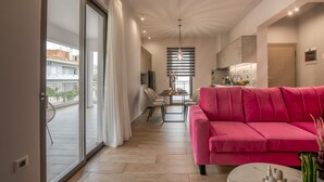 A modern living room with a pink sofa, a dining area with a table and chairs, and a kitchen in the background. - MAGNOLIA Luxury Chania Central Apartments (Chania)