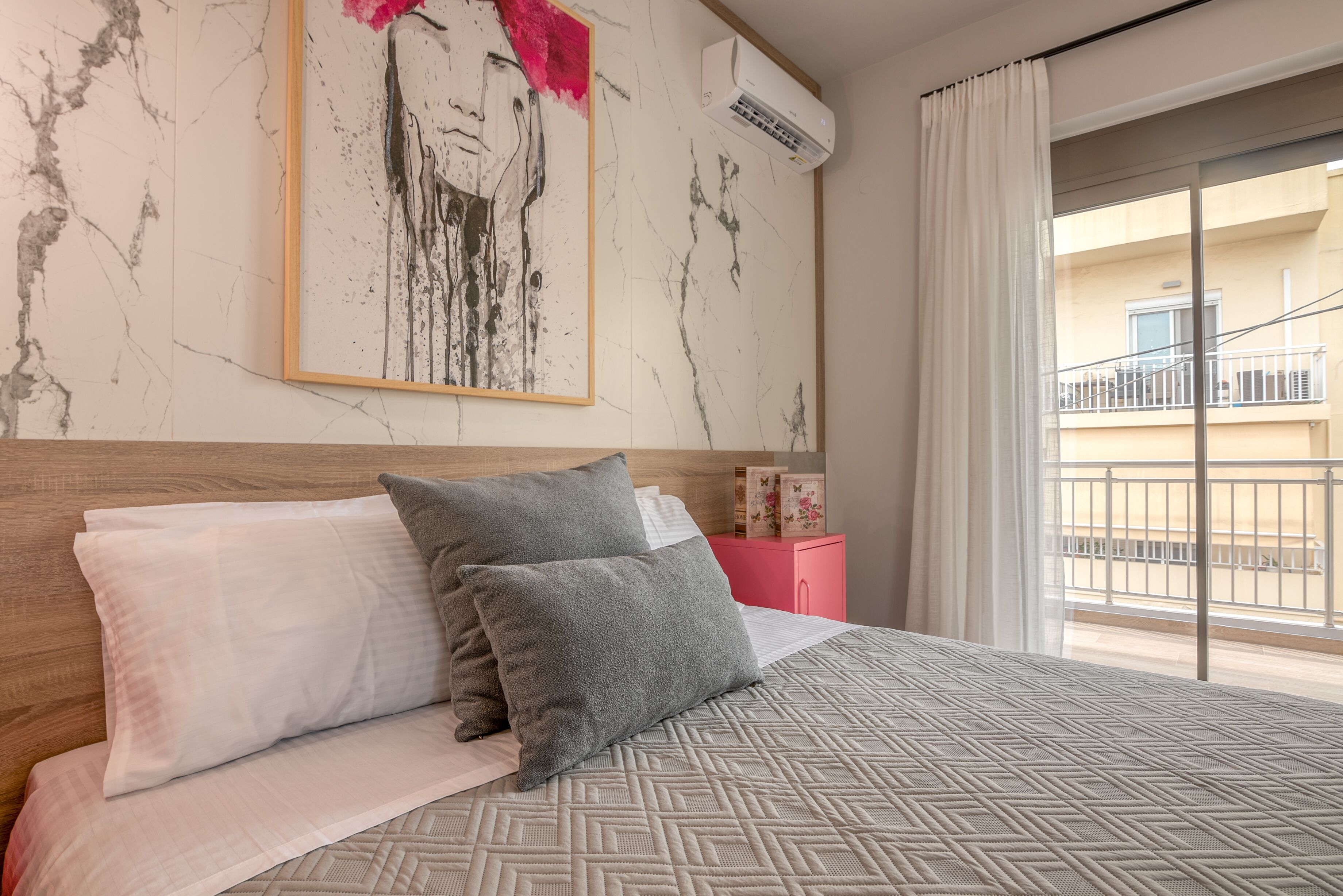 Una habitación de hotel con una cama, una obra de arte enmarcada, un equipo de aire acondicionado y vistas al balcón exterior.