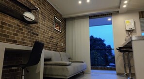 Un salon moderne avec un canapé, un fauteuil, une horloge et une fenêtre donnant sur un balcon.