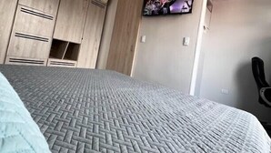 Une chambre avec un lit, un ventilateur de plafond, une armoire en bois et un téléviseur fixé au mur.