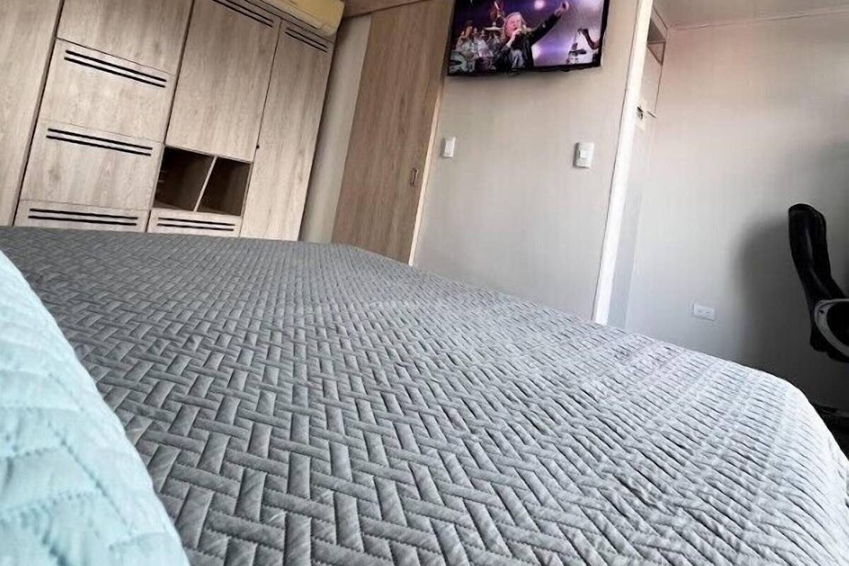 Un dormitorio con cama, ventilador de techo, armario de madera y televisor en la pared.