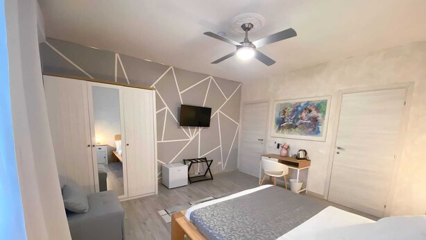 Ein modernes Schlafzimmer mit einem Bett, einem Schreibtisch, einem Sessel, einem Fernseher und einem Deckenventilator.