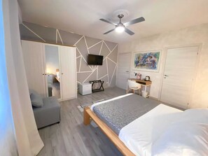 A modern bedroom with a bed, a desk, a chair, a TV, and a ceiling fan. - Bed breakfast Relais Delta (Taglio di Po)