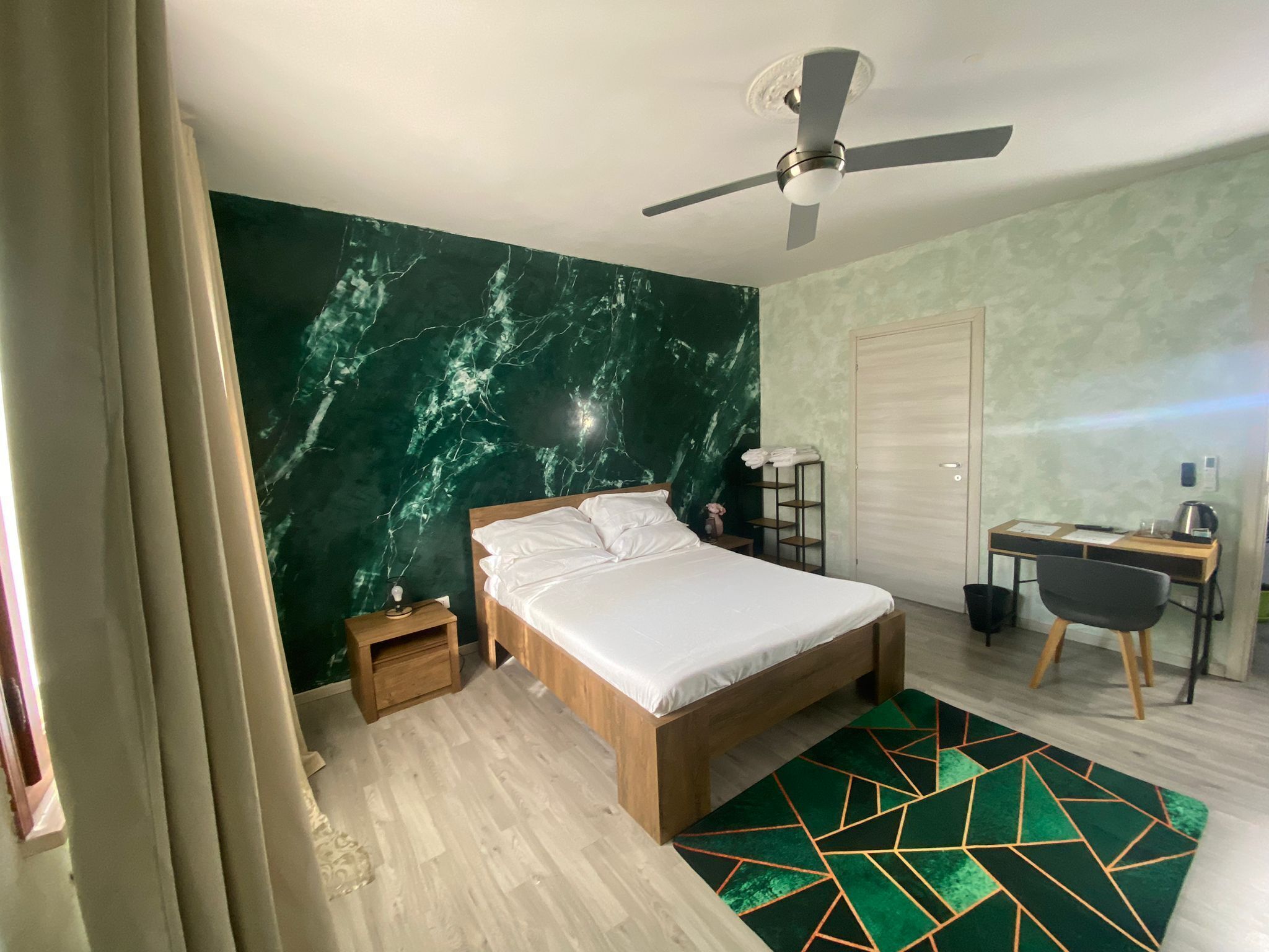 Ein Schlafzimmer mit Bett, Schreibtisch, Stuhl, Deckenventilator und einer Wand aus grünem Marmor.