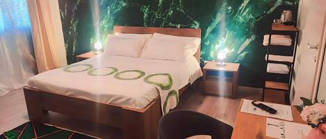 Une chambre à coucher comprenant un lit, des tables de chevet, une chaise, un bureau et un mur orné d’un motif végétal vert.