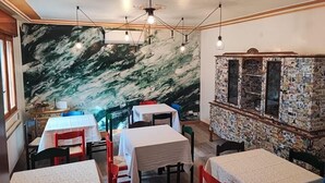 Ein Restaurantinneres mit Marmor-Wandgemälden, mehreren Tischen mit weißen Tischdecken und hängenden Pendelleuchten.
