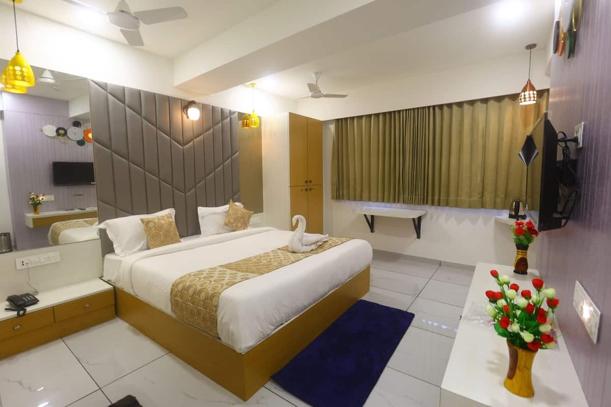 Une chambre d’hôtel avec un grand lit, une table de chevet, un miroir, une télévision, un ventilateur de plafond et une fenêtre avec des rideaux.