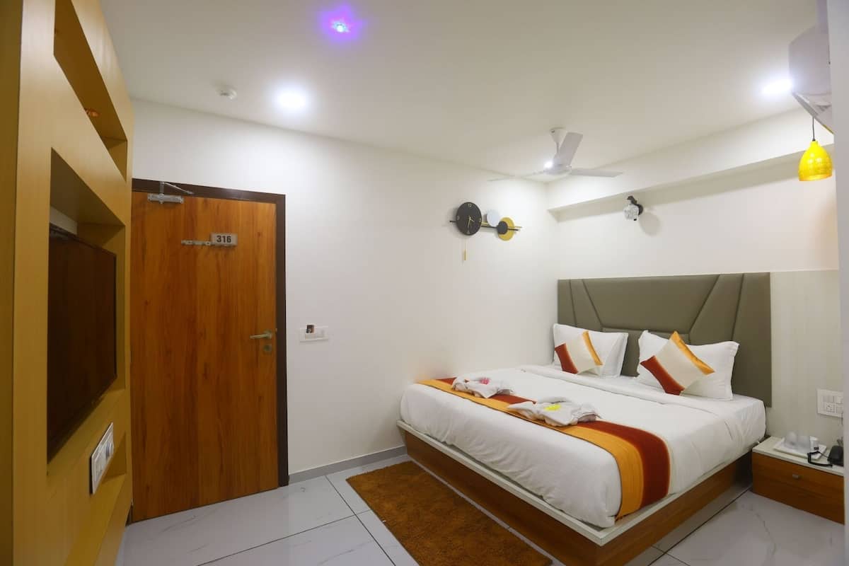 Une chambre d’hôtel avec un lit, une porte en bois, une horloge, un ventilateur de plafond et une table de chevet.