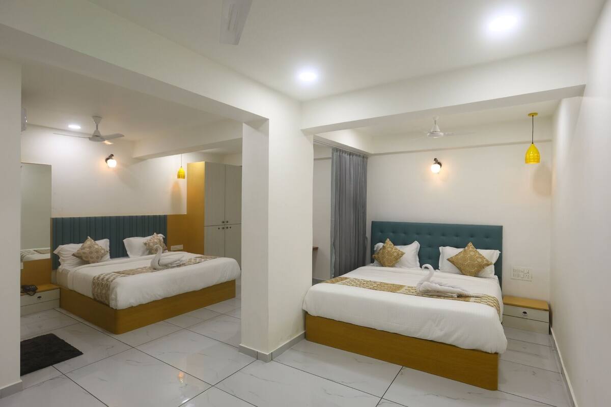 Une chambre d’hôtel avec deux lits, chacun doté d’une tête de lit bleue, de draps blancs et d’oreillers décoratifs. La chambre est également équipée de ventilateurs de plafond, de lampes murales et d’un miroir.