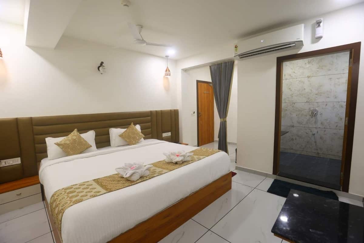 Une chambre d’hôtel avec un grand lit, une tête de lit en bois, une table de chevet, un climatiseur, une armoire et une salle de bain carrelée.