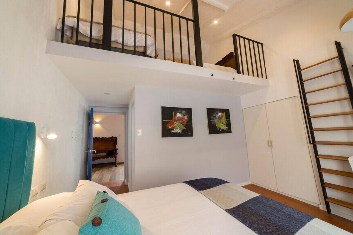 A bedroom with a bed, a staircase, a wardrobe, and two framed pictures on the wall.