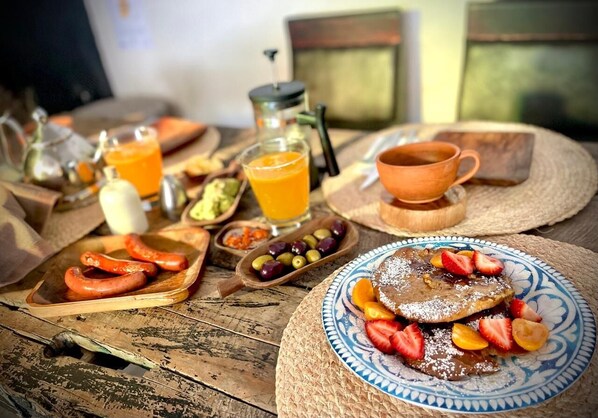Una mesa de madera rústica con alimentos para el desayuno, como tortitas, salchichas y fruta fresca.