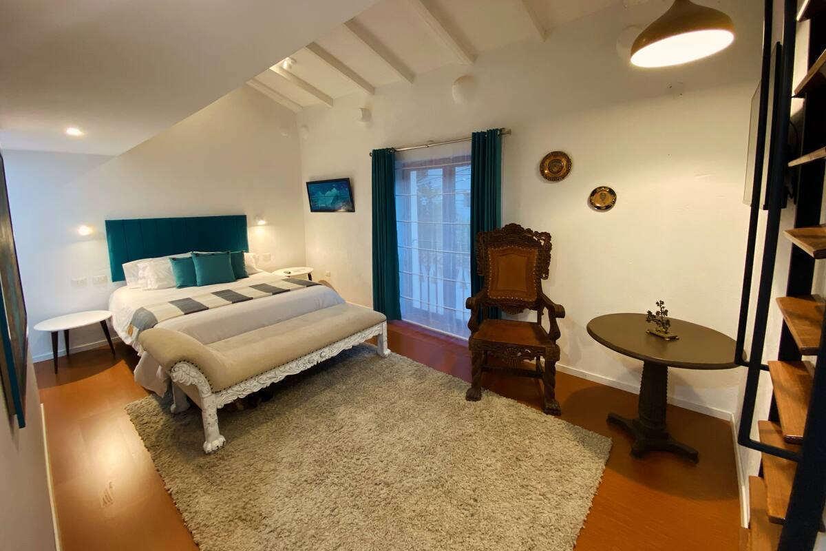 A bedroom with a bed, a small round table, a chair, and a television on the wall.