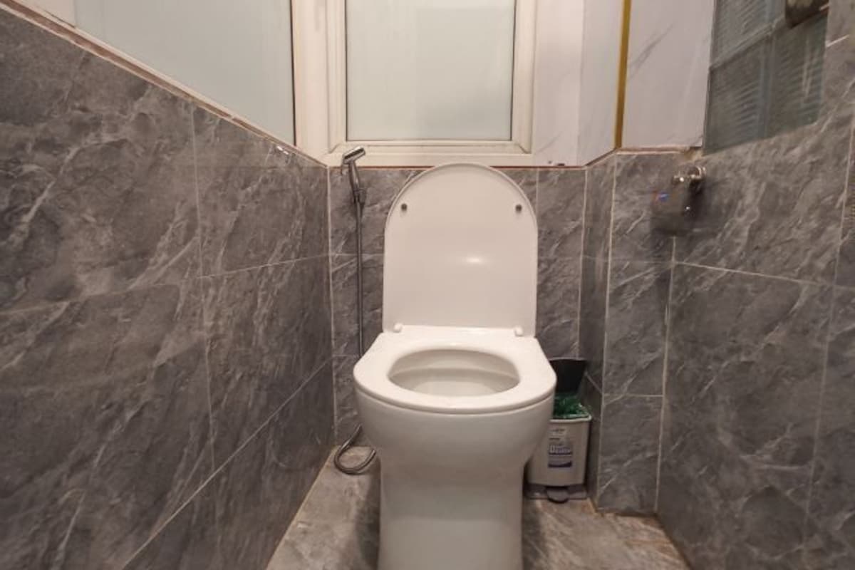 A bathroom with a white toilet, marble walls, and a cabinet above the toilet.