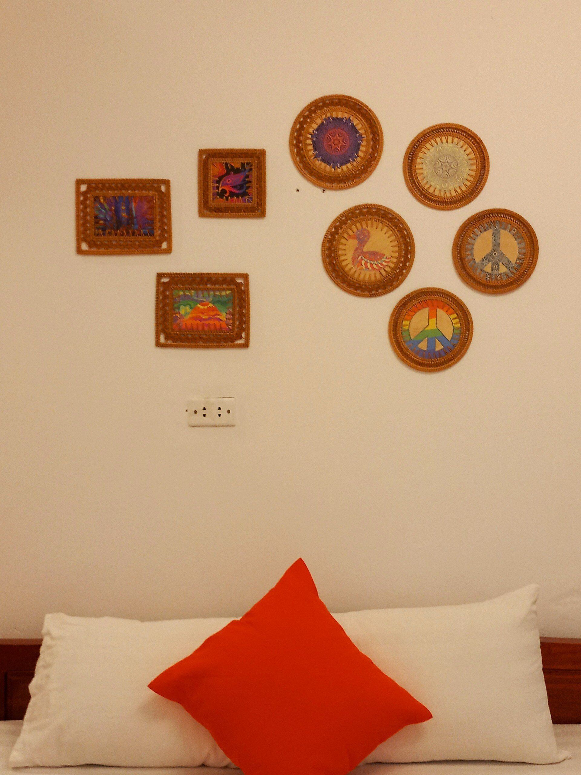 A wall with six woven wall hangings and a bed with a white pillow and a red accent pillow.
