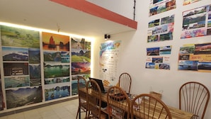 A dining area with a wooden table and chairs, a menu board, and a wall decorated with travel posters. - Hanowood Homestay & Travel (Hanoi)