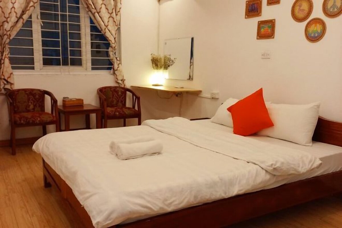A hotel room with a bed, a desk, two chairs, and a window with curtains.