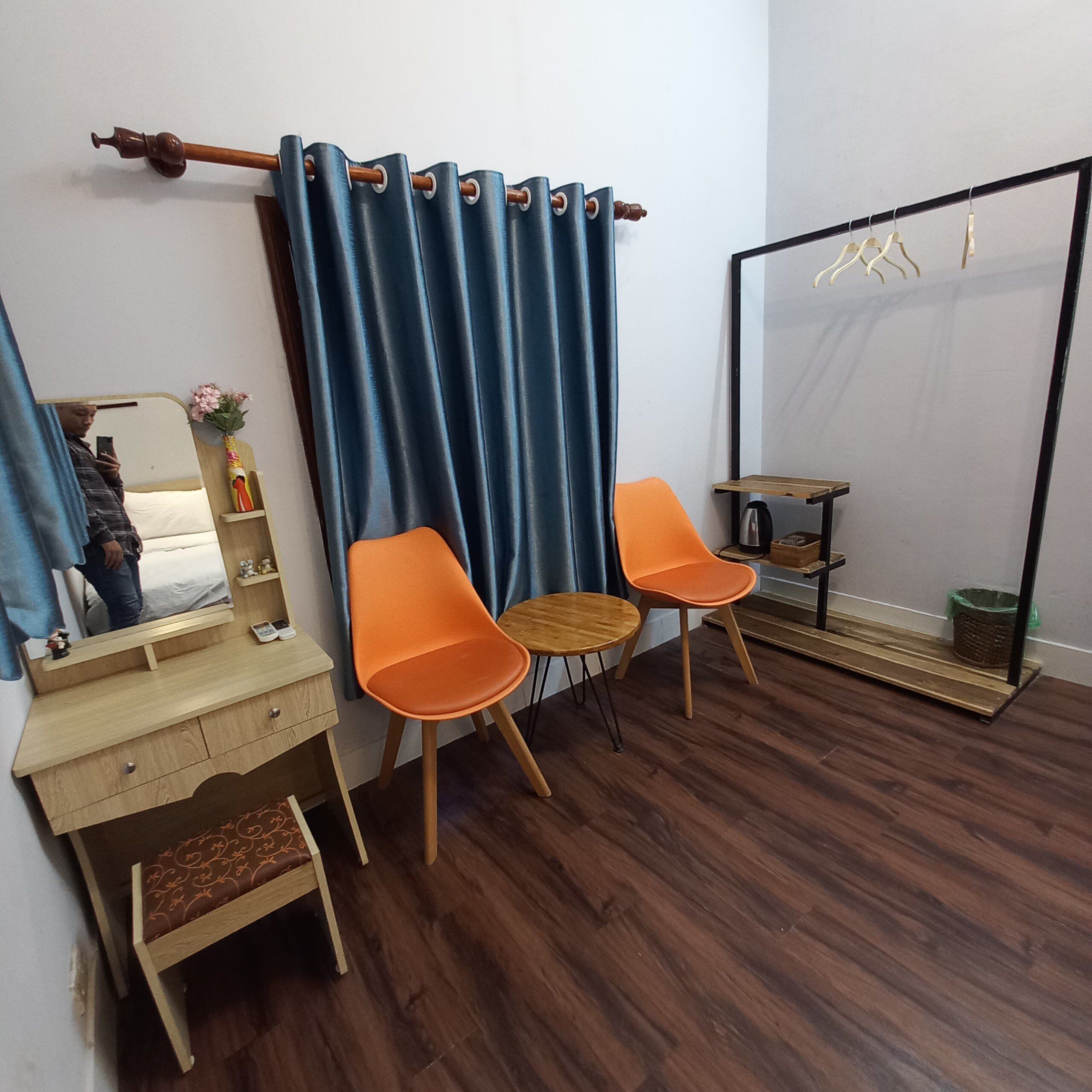 Una habitación con un escritorio de madera, dos sillas naranjas, un espejo y una cortina azul.