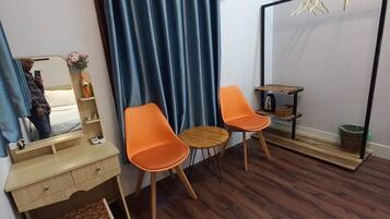Una habitación con un escritorio de madera, dos sillas naranjas, un espejo y una cortina azul.