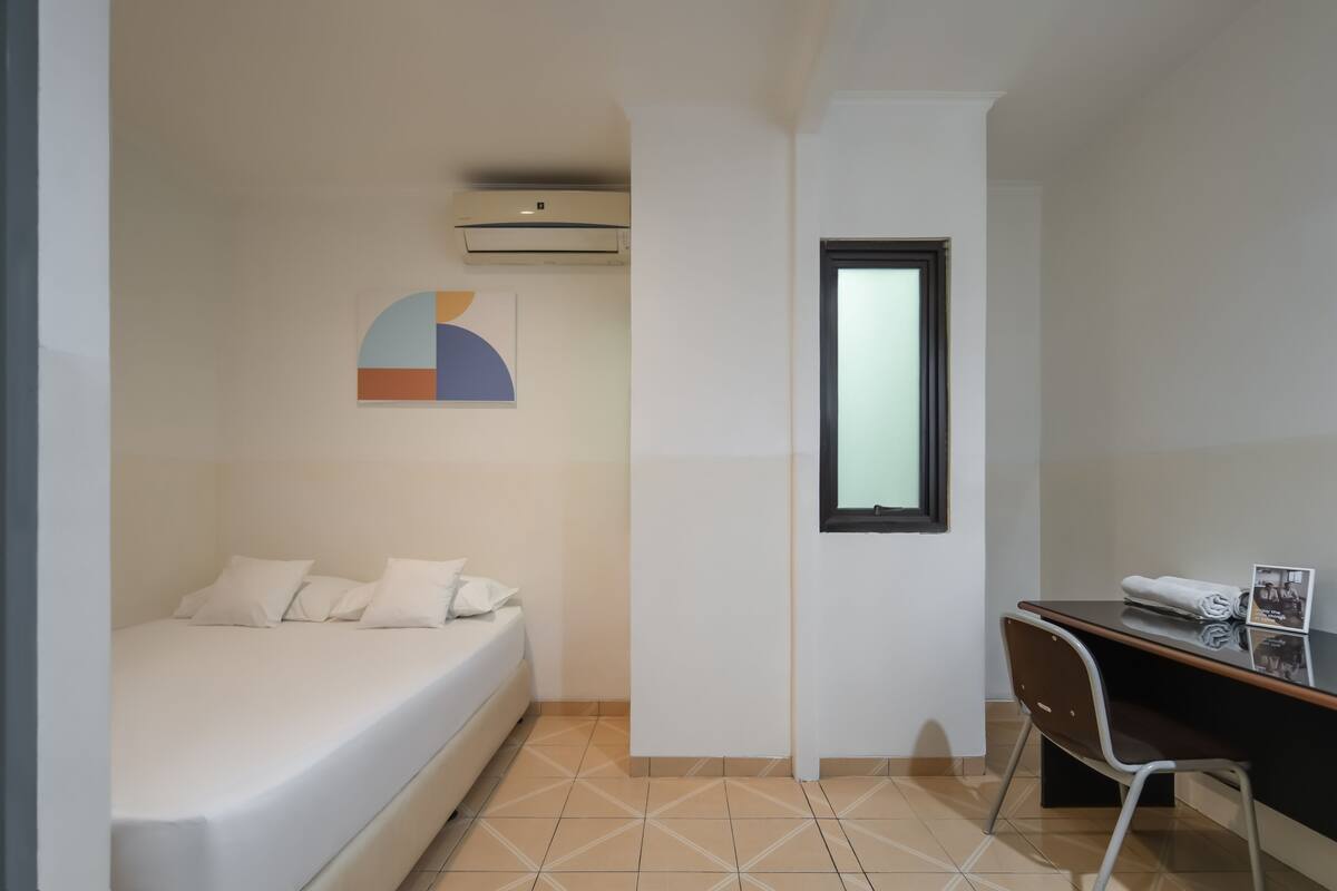 A small, clean room with a bed, a desk, and a window.