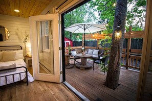 Una habitación con cama, techo de madera y una puerta corrediza de vidrio que da a un patio exterior con mesa, sillas y una sombrilla.