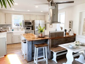 A modern kitchen with white cabinetry, stainless steel appliances, a wooden island with stools, and a ceiling fan. - Farmhouse & Cottage near DT, USC (Lexington County)