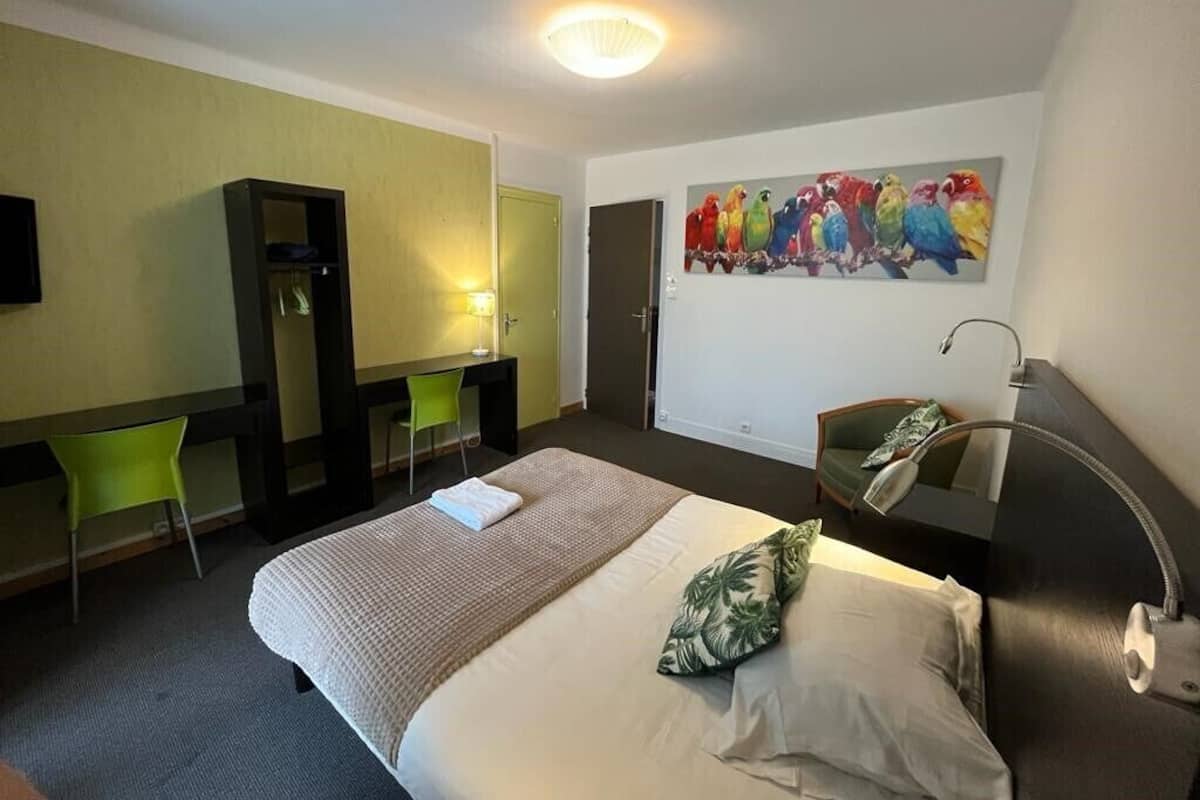 A hotel room with a bed, a desk, a chair, a painting, and a lamp.