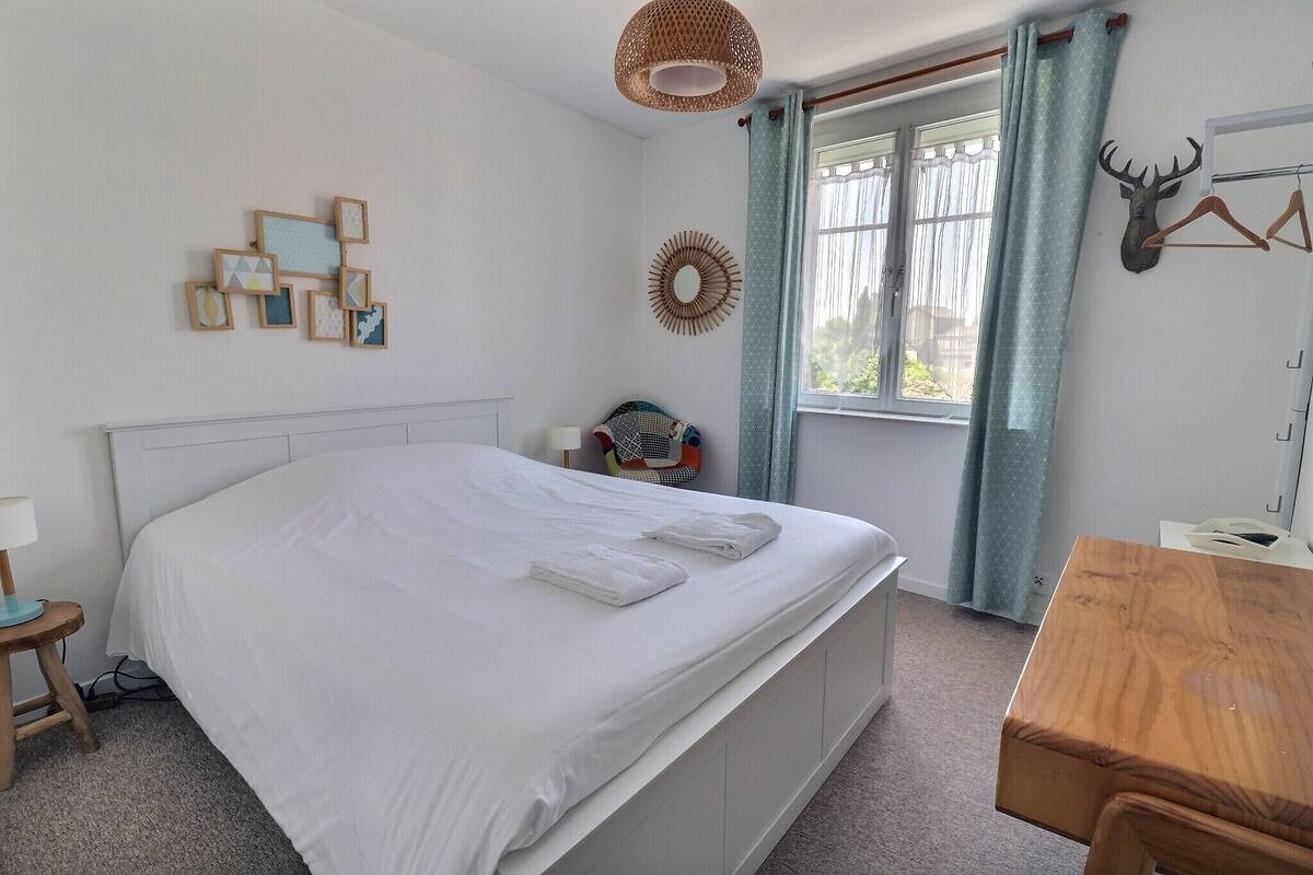 A neatly made bed with white linens, a wooden headboard, a wall-mounted mirror, a decorative wall piece, and a deer head on a wall.
